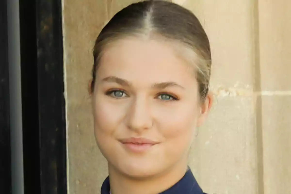 La princesa Leonor amb els cabells rossos recollits i els ulls clars somrient lleument davant d’una paret de pedra