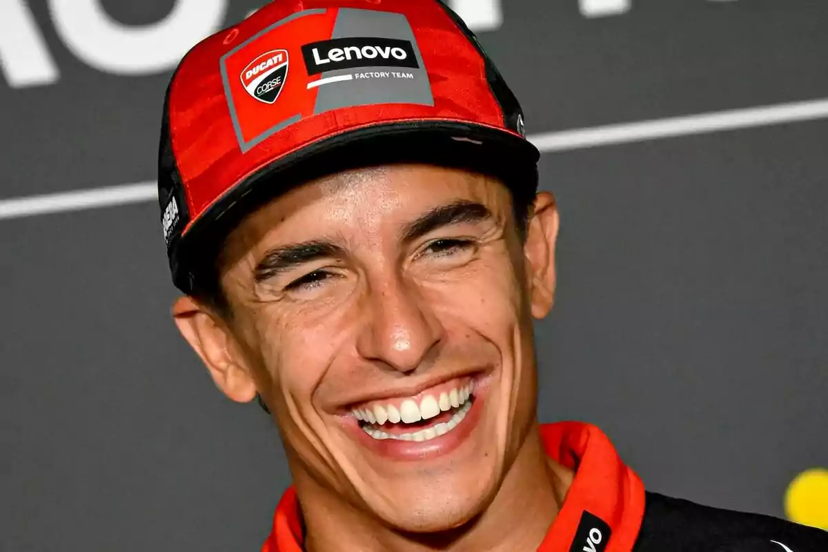 Primer plano de Marc Márquez con gorra roja de Ducati y camiseta a juego sonriendo ampliamente. Primer plano de Marc Márquez con gorra roja de Ducati y camiseta a juego sonriendo ampliamente.