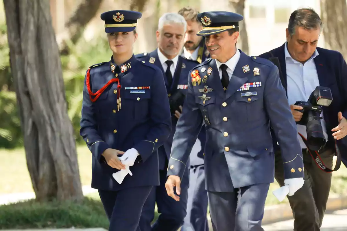 Diverses persones amb uniformes militars caminen a l’aire lliure mentre un home amb càmera les acompanya. Diverses persones amb uniformes militars caminen a l’aire lliure mentre un home amb càmera les acompanya.