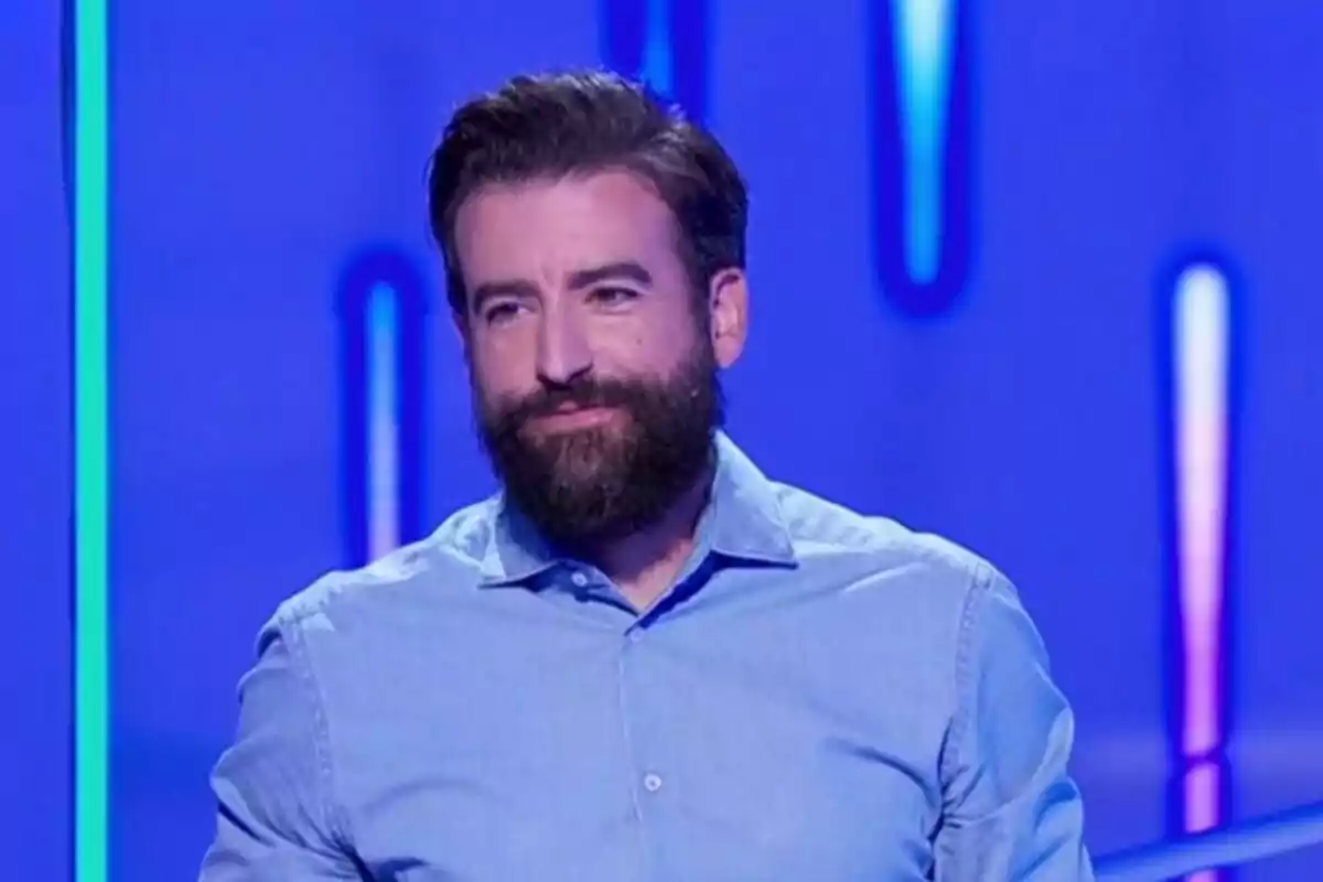 Rafa Castaño amb barba i cabell fosc amb camisa blau clar en un fons blau amb llums verticals difuses. Rafa Castaño amb barba i cabell fosc amb camisa blau clar en un fons blau amb llums verticals difuses.