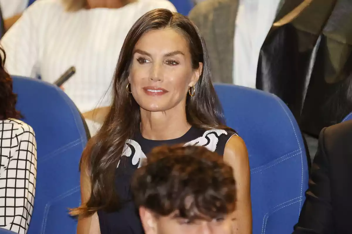 La reina Letizia sentada en una butaca azul durante un evento formal rodeada de otras personas La reina Letizia sentada en una butaca azul durante un evento formal rodeada de otras personas