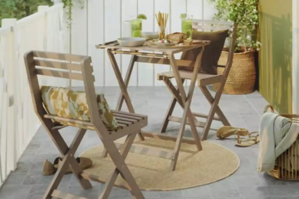 Joc de taula i dues cadires de fusta en un balcó decorat amb coixins, begudes i menjar sobre la taula, plantes i objectes personals al voltant. Joc de taula i dues cadires de fusta en un balcó decorat amb coixins, begudes i menjar sobre la taula, plantes i objectes personals al voltant.