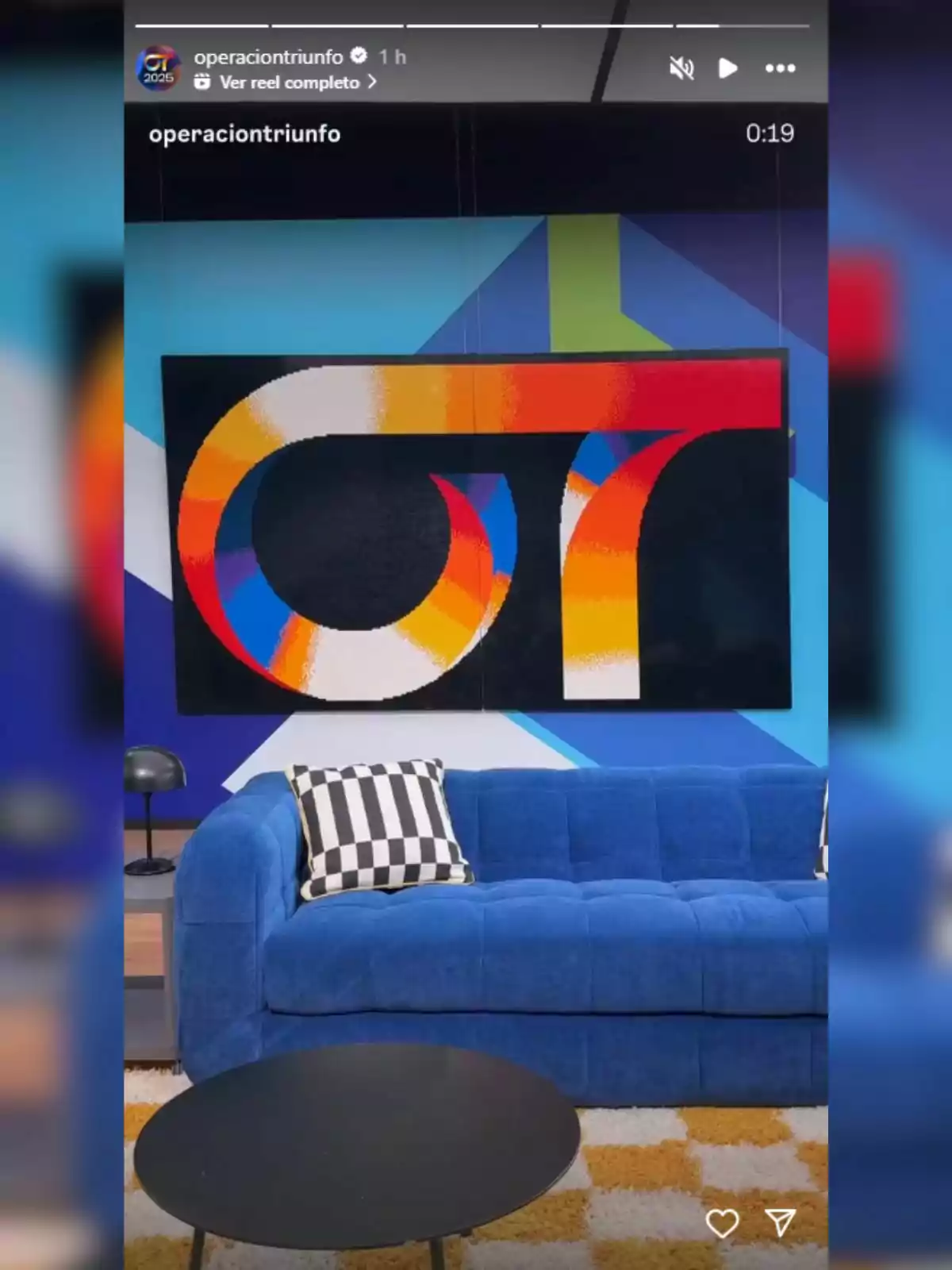 Sofá azul con cojines de cuadros en blanco y negro frente a una mesa redonda negra y una pared decorada con un cuadro colorido y diseño geométrico