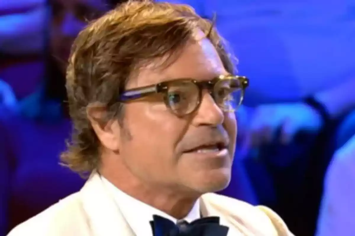 Home amb ulleres i llacet parlant en un programa de televisió amb un fons blau desenfocat. Captura de 'Supervivientes'