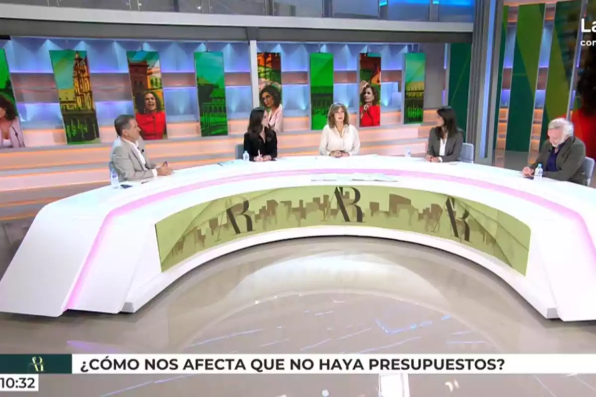 Cinc persones assegudes al voltant d’una taula semicircular en un plató de televisió amb pantalles de fons i un rètol a la part inferior que pregunta com afecta la manca de pressupostos. Captura de ‘El Programa de AR’. Cinc persones assegudes al voltant d’una taula semicircular en un plató de televisió amb pantalles de fons i un rètol a la part inferior que pregunta com afecta la manca de pressupostos. Captura de ‘El Programa de AR’.
