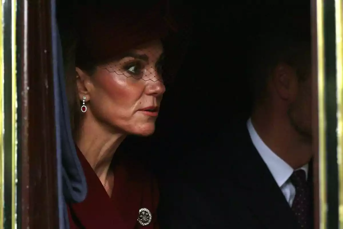 Dona elegantment vestida amb barret i vel fosc asseguda al costat d’un home en un ambient tènue Dona elegantment vestida amb barret i vel fosc asseguda al costat d’un home en un ambient tènue