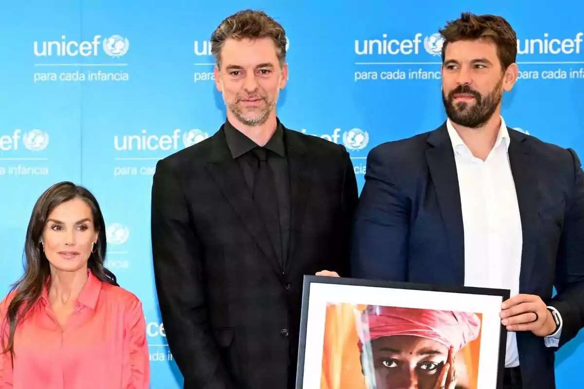 Tres personas posan frente a un fondo azul de UNICEF, una de ellas sostiene una fotografía enmarcada de una mujer con un pañuelo rosa. Tres personas posan frente a un fondo azul de UNICEF, una de ellas sostiene una fotografía enmarcada de una mujer con un pañuelo rosa.