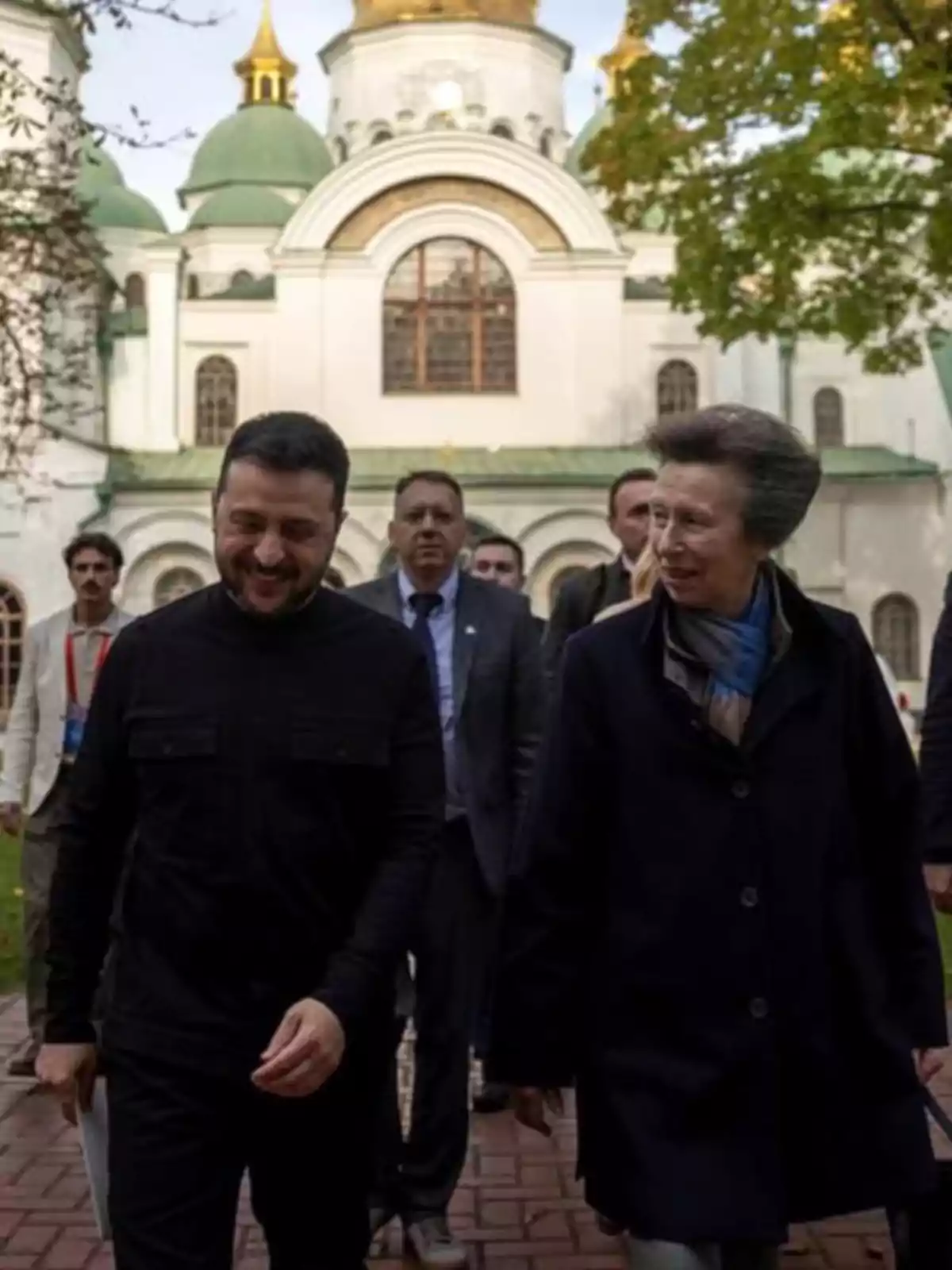 Diverses persones caminen i conversen davant d’un edifici històric amb cúpules verdes i daurades.