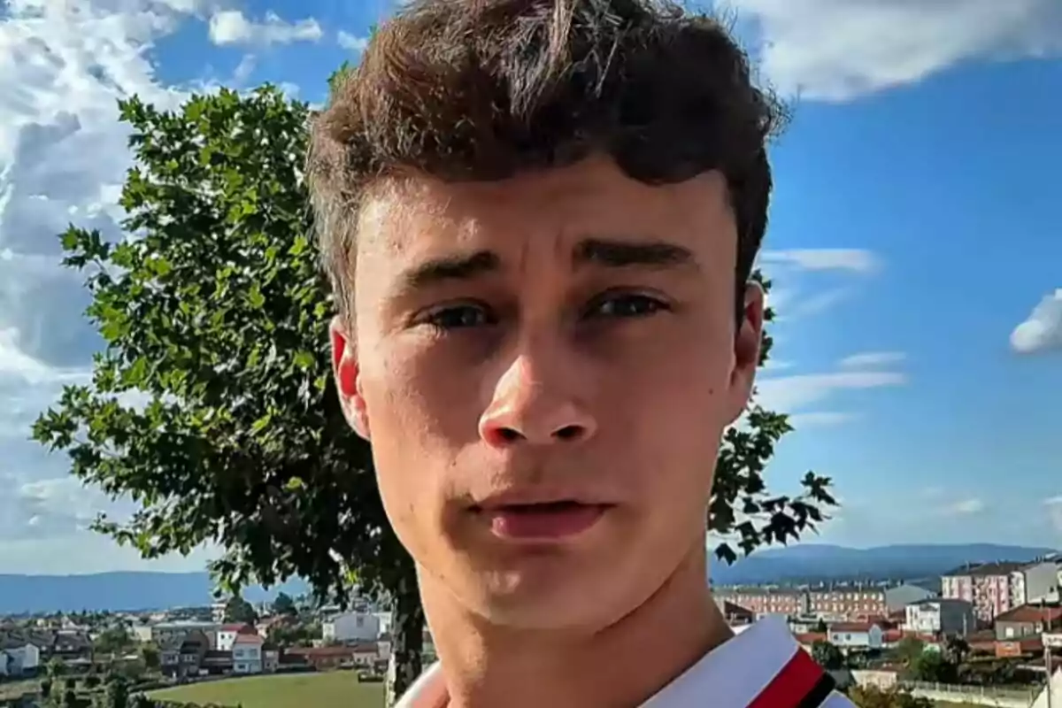 Primer pla de Jorge Rey mirant a la càmera amb un paisatge urbà i muntanyes al fons en un dia assolellat.