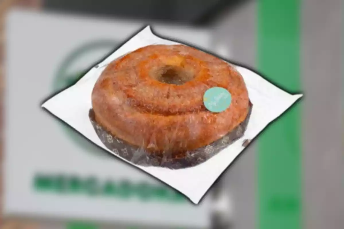 Pastís tipus rosca embolicat en plàstic sobre un fons borros amb colors verd i gris