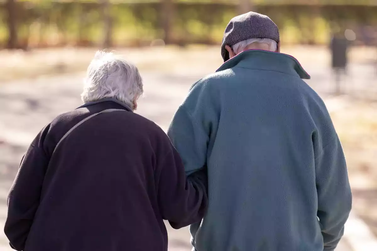 Dues persones grans caminant juntes a l’aire lliure, una d’elles sosté el braç de l’altra en senyal de suport. Dues persones grans caminant juntes a l’aire lliure, una d’elles sosté el braç de l’altra en senyal de suport.