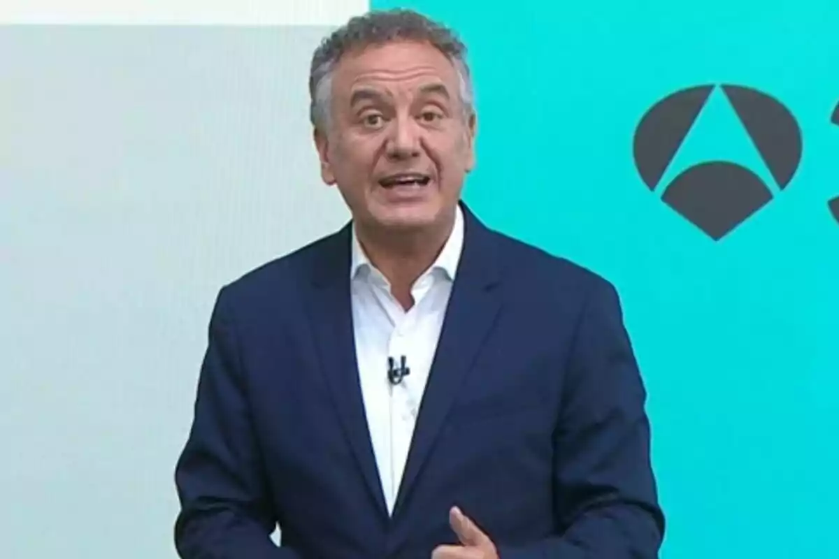 Home de cabells canosos, que és Roberto Brasero, vestit amb un vestit blau i camisa blanca parlant davant d’un fons blau amb logotips geomètrics negres.