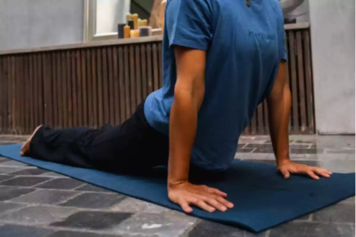 Persona practicant ioga sobre una estoreta blava fent la postura de la cobra en un espai interior