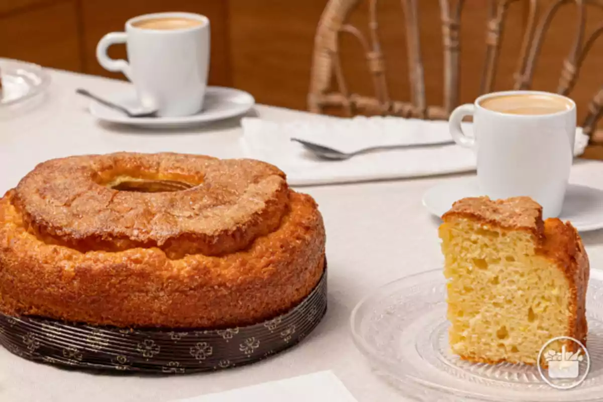 Pa de pessic esponjós amb sucre per sobre acompanyat de dues tasses de cafè sobre una taula amb estovalla blanca