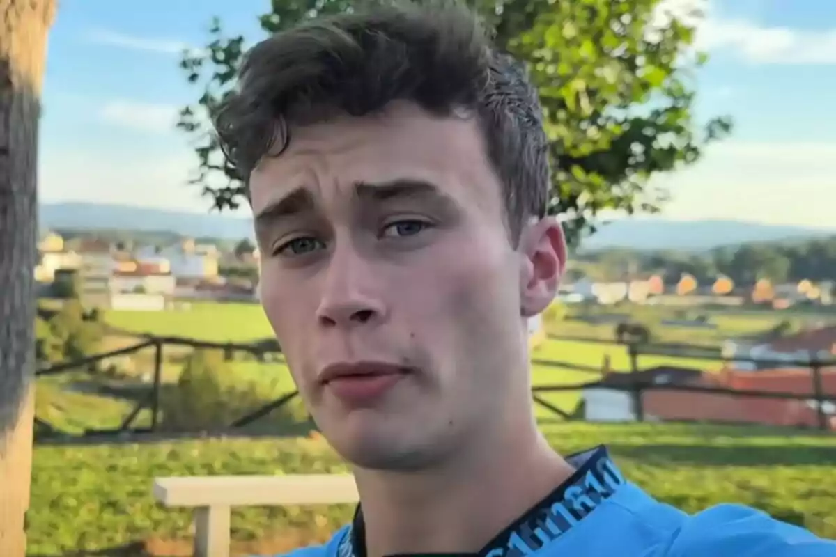 Jove de cabell curt i ulls clars, que és Jorge Rey, posant a l’aire lliure amb un paisatge de camp i cases al fons.