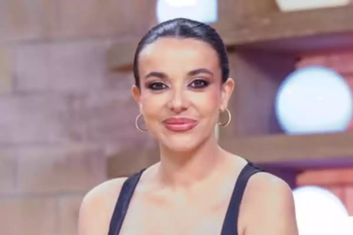 Sarah Santaolalla, con cabello oscuro recogido con maquillaje elegante y pendientes de aro posando y sonriendo, en un plató de televisión Sarah Santaolalla, con cabello oscuro recogido con maquillaje elegante y pendientes de aro posando y sonriendo, en un plató de televisión