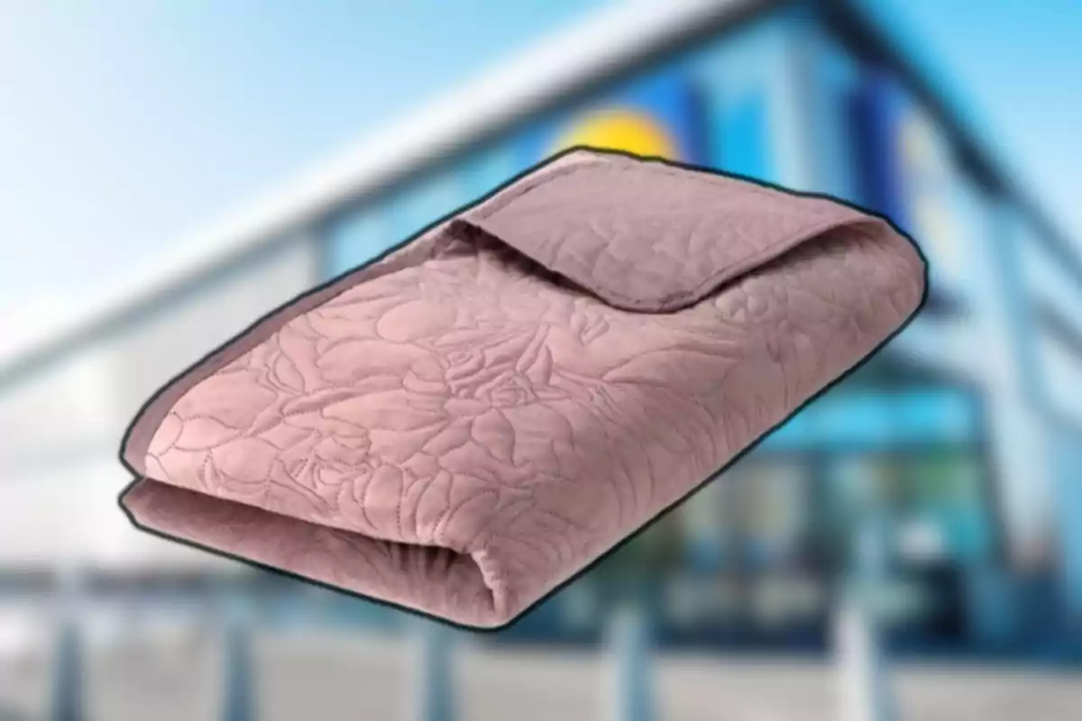 Manta rosa doblada con diseño de flores en relieve frente a un edificio desenfocado Manta rosa doblada con diseño de flores en relieve frente a un edificio desenfocado