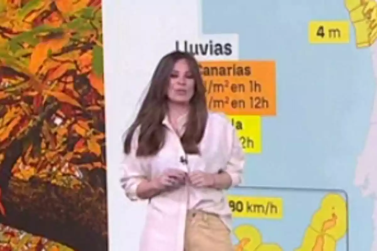 Mercedes Martín de pie frente a un mapa meteorológico con información sobre lluvias y viento, vistiendo camisa clara y pantalón beige. Mercedes Martín de pie frente a un mapa meteorológico con información sobre lluvias y viento, vistiendo camisa clara y pantalón beige.
