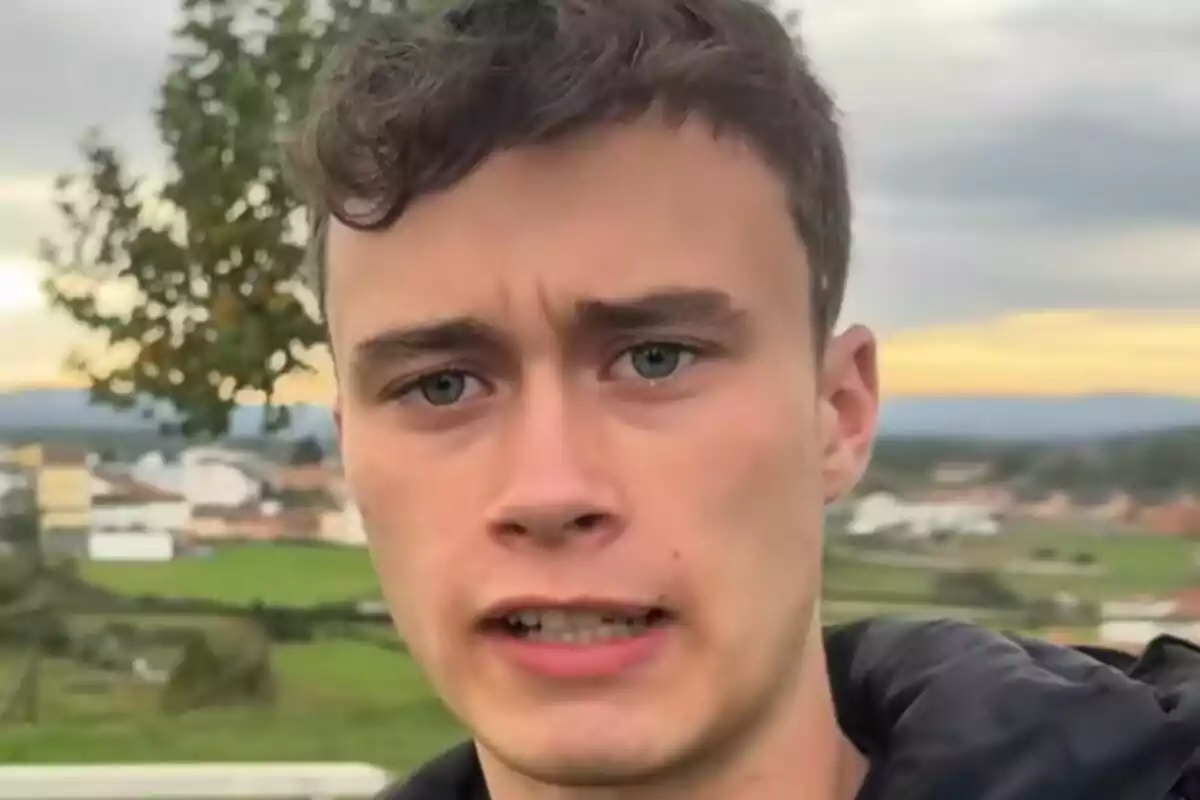 Jorge Rey amb expressió seriosa a l’aire lliure, amb un paisatge de camp i cases al fons.