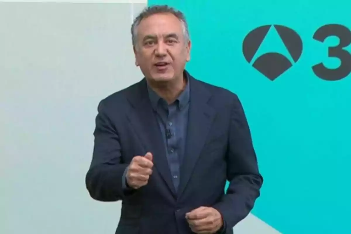 Roberto Brasero vestit amb un vestit blau fosc parlant davant d’un fons turquesa amb un logotip.