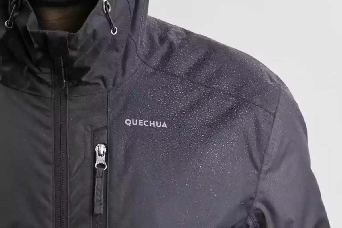 Una jaqueta negra impermeable de la marca Quechua amb gotes d'aigua a la superfície.