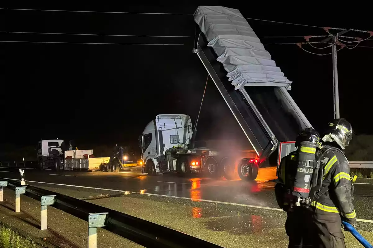 Bombers treballant a l'escena d'un accident de camió a una carretera durant la nit.