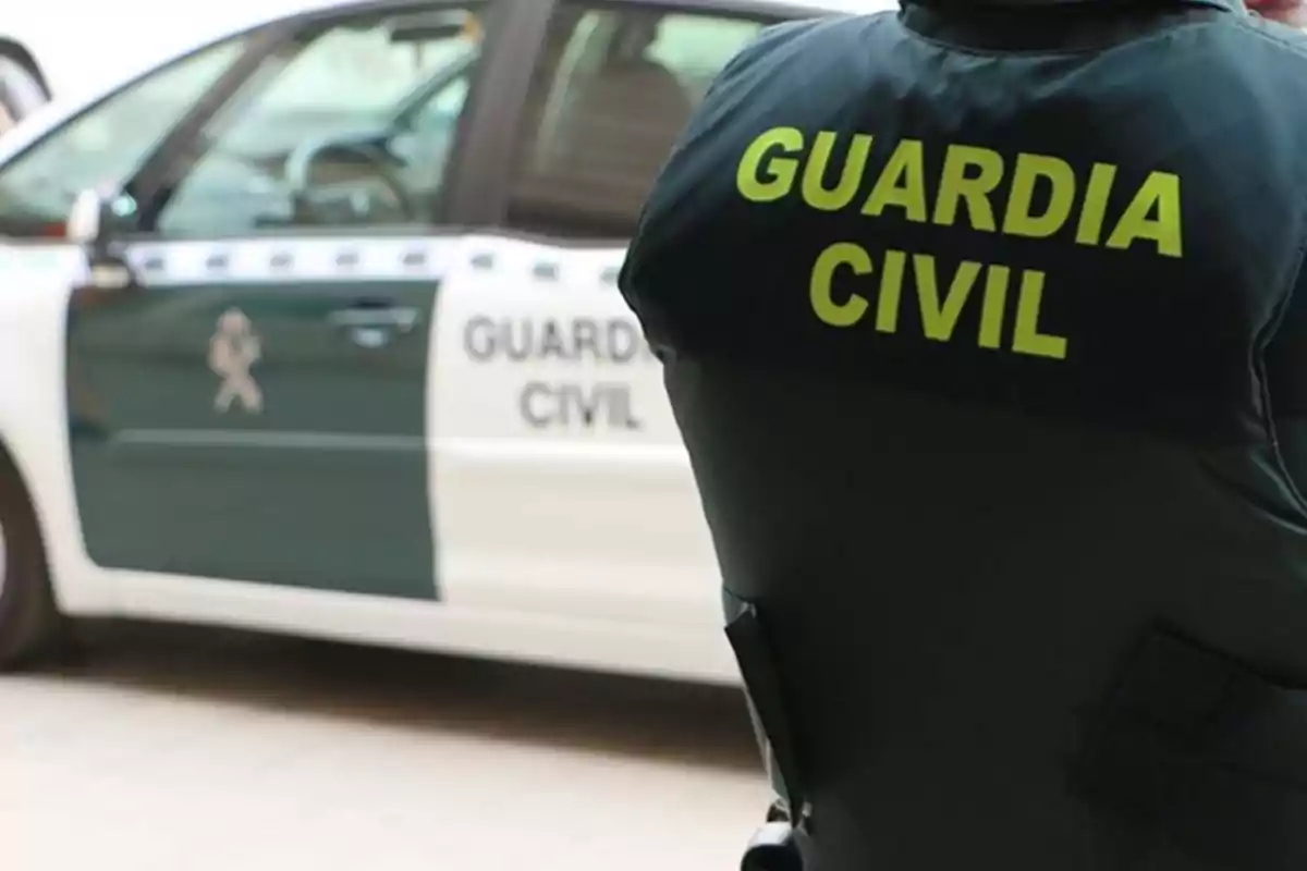 Agent de la Guàrdia Civil d?esquena al costat d?un cotxe patrulla.