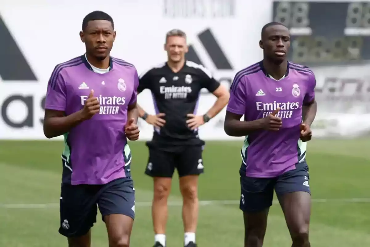 Two Real Madrid football players training in purple jerseys while a coach watches them in the background.