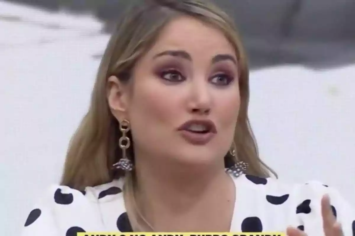 Alba Carrillo amb cabell ros i maquillatge cridaner està parlant, porta una brusa blanca amb topos negres i arracades grans a La Família de la Tele.
