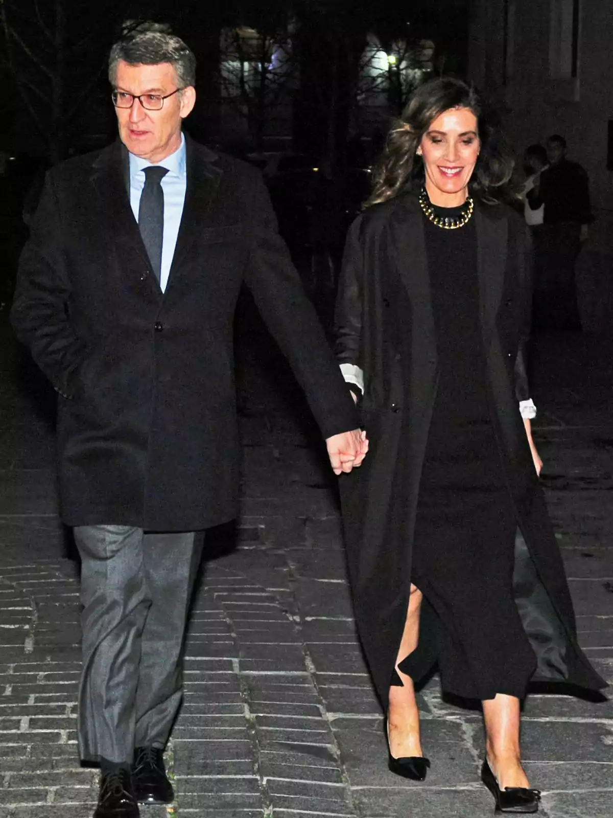 Alberto Núñez Feijóo y Eva Cárdenas caminando de noche, ambos vestidos formalmente y tomados de la mano. Alberto Núñez Feijóo y Eva Cárdenas caminando de noche, ambos vestidos formalmente y tomados de la mano.
