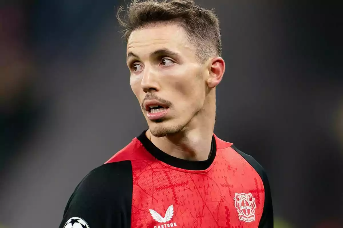 Un jugador de futbol amb uniforme vermell i negre del Bayer Leverkusen mira cap a un costat durant un partit. Un jugador de futbol amb uniforme vermell i negre del Bayer Leverkusen mira cap a un costat durant un partit.
