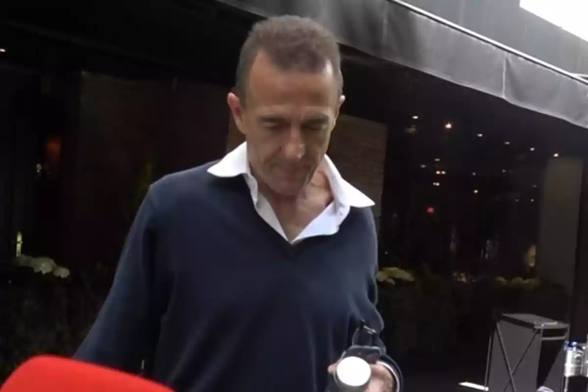 Alessandro Lequio amb camisa blanca i jersei fosc sosté un objecte mentre camina davant d'un edifici amb llums. Alessandro Lequio amb camisa blanca i jersei fosc sosté un objecte mentre camina davant d'un edifici amb llums.