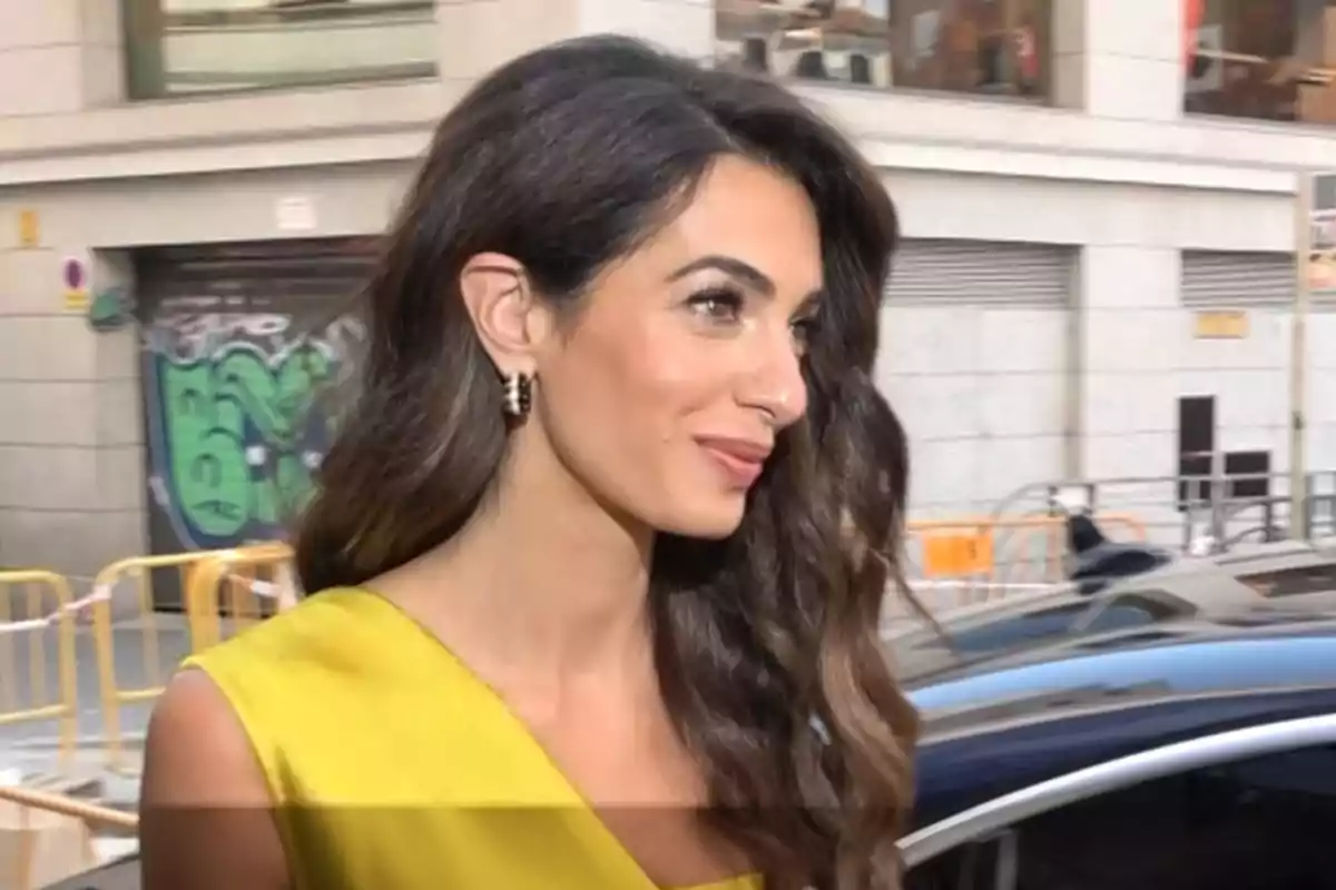 Amal Clooney in a yellow dress with her hair down walking down the street. Amal Clooney in a yellow dress with her hair down walking down the street.