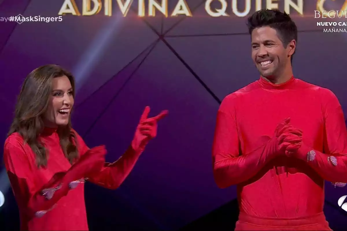 Ana Boyer i Fernando Verdasco vestides amb vestits vermells somriuen en un escenari de Mask Singer amb el text Ana Boyer i Fernando Verdasco vestides amb vestits vermells somriuen en un escenari de Mask Singer amb el text