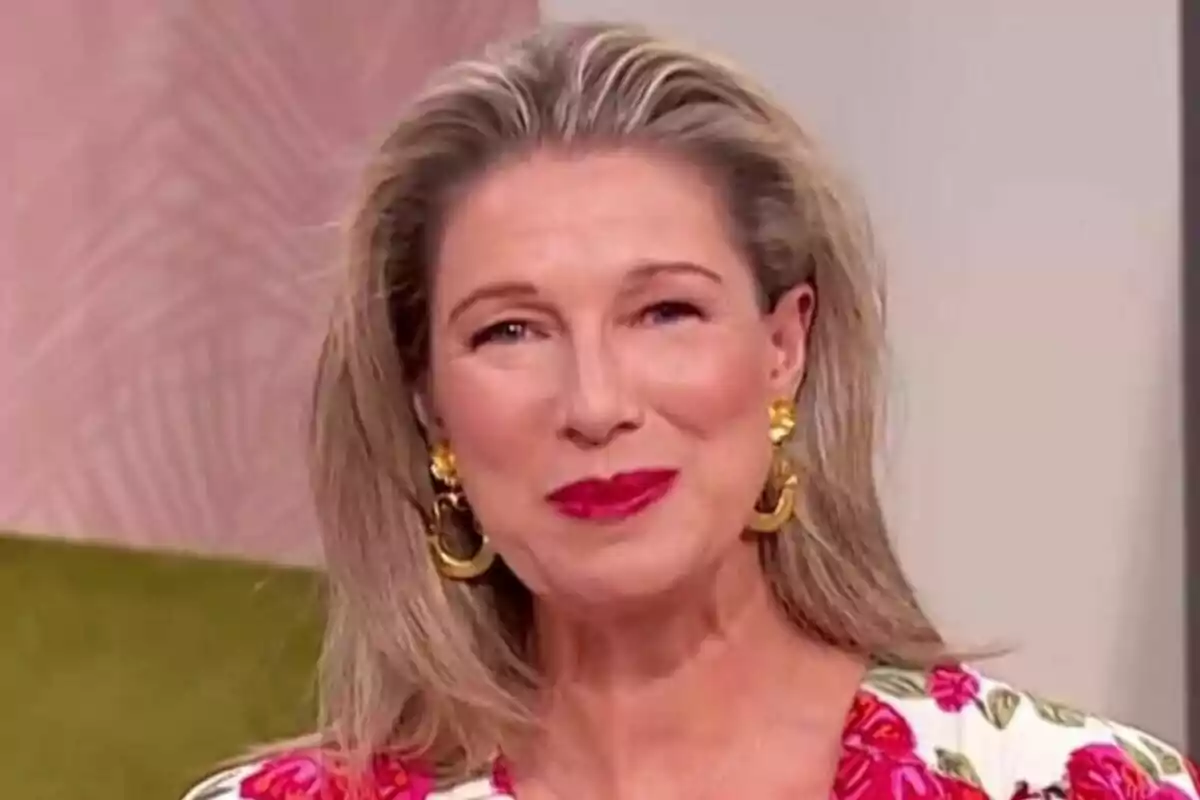 Anne Igartiburu de cabello rubio y largo con labios rojos, usando aretes dorados grandes y blusa con estampado floral, sonríe frente a un fondo claro en D Corazón Anne Igartiburu de cabello rubio y largo con labios rojos, usando aretes dorados grandes y blusa con estampado floral, sonríe frente a un fondo claro en D Corazón