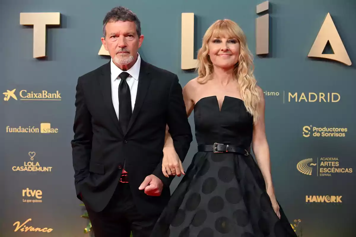 Antonio Banderas i Cayetana Guillén Cuervo elegantment vestida posen en una catifa vermella davant d'un fons amb logotips de patrocinadors. Antonio Banderas i Cayetana Guillén Cuervo elegantment vestida posen en una catifa vermella davant d'un fons amb logotips de patrocinadors.
