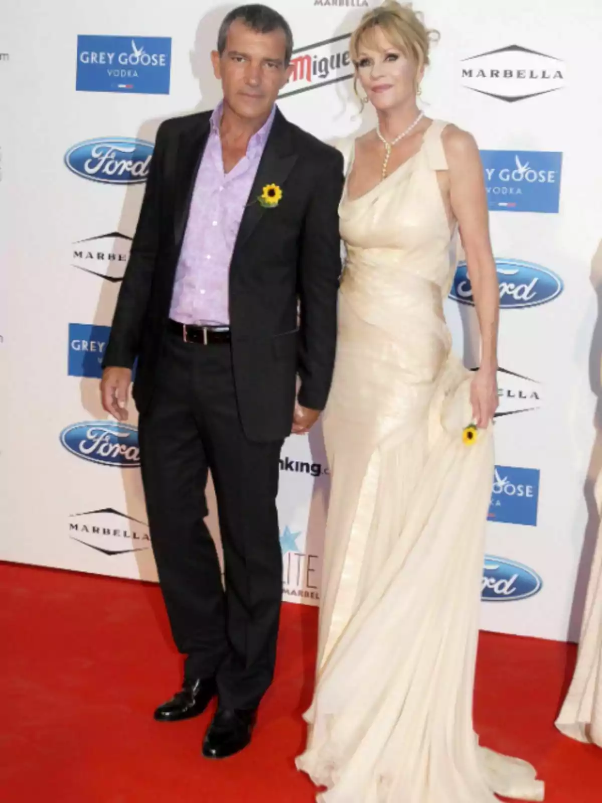 Antonio Banderas i Melanie Griffith posant en una catifa vermella amb un fons de logotips de marques. Antonio Banderas i Melanie Griffith posant en una catifa vermella amb un fons de logotips de marques.