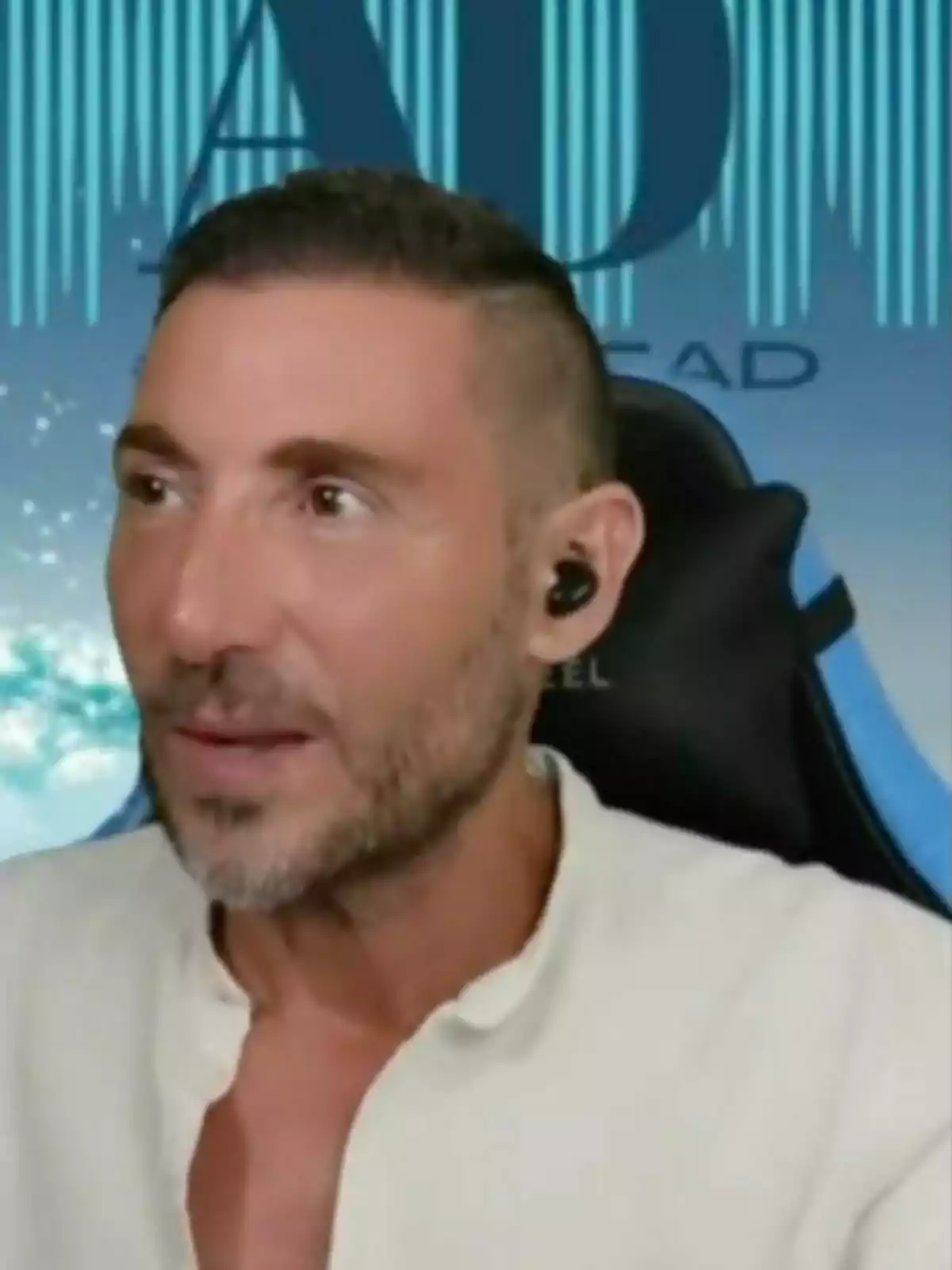 Antonio David Flores amb auriculars negres i camisa blanca, assegut davant d'un fons blau amb lletres. Antonio David Flores amb auriculars negres i camisa blanca, assegut davant d'un fons blau amb lletres.