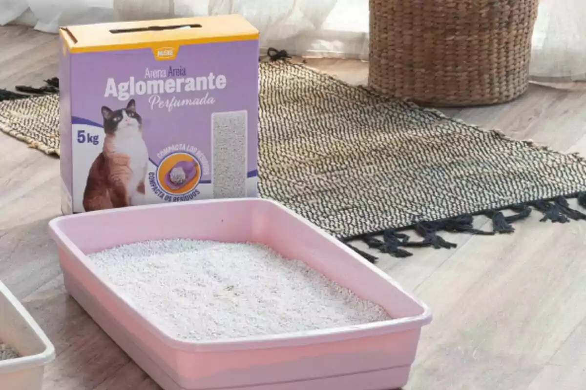 Caixa de sorra aglomerant per a gats al costat d’una safata higiènica rosa amb sorra a l’interior sobre un terra de fusta i una catifa de punt. Caixa de sorra aglomerant per a gats al costat d’una safata higiènica rosa amb sorra a l’interior sobre un terra de fusta i una catifa de punt.
