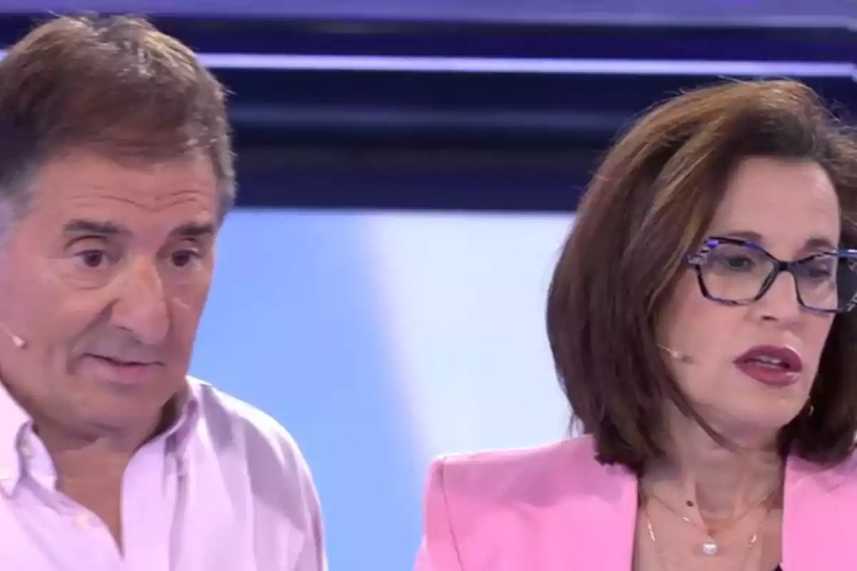 Dues persones en un set de televisió, una dona amb ulleres i jaqueta rosa i un home amb camisa clara, tots dos amb micròfons. Captura d''Atrapa un millón'