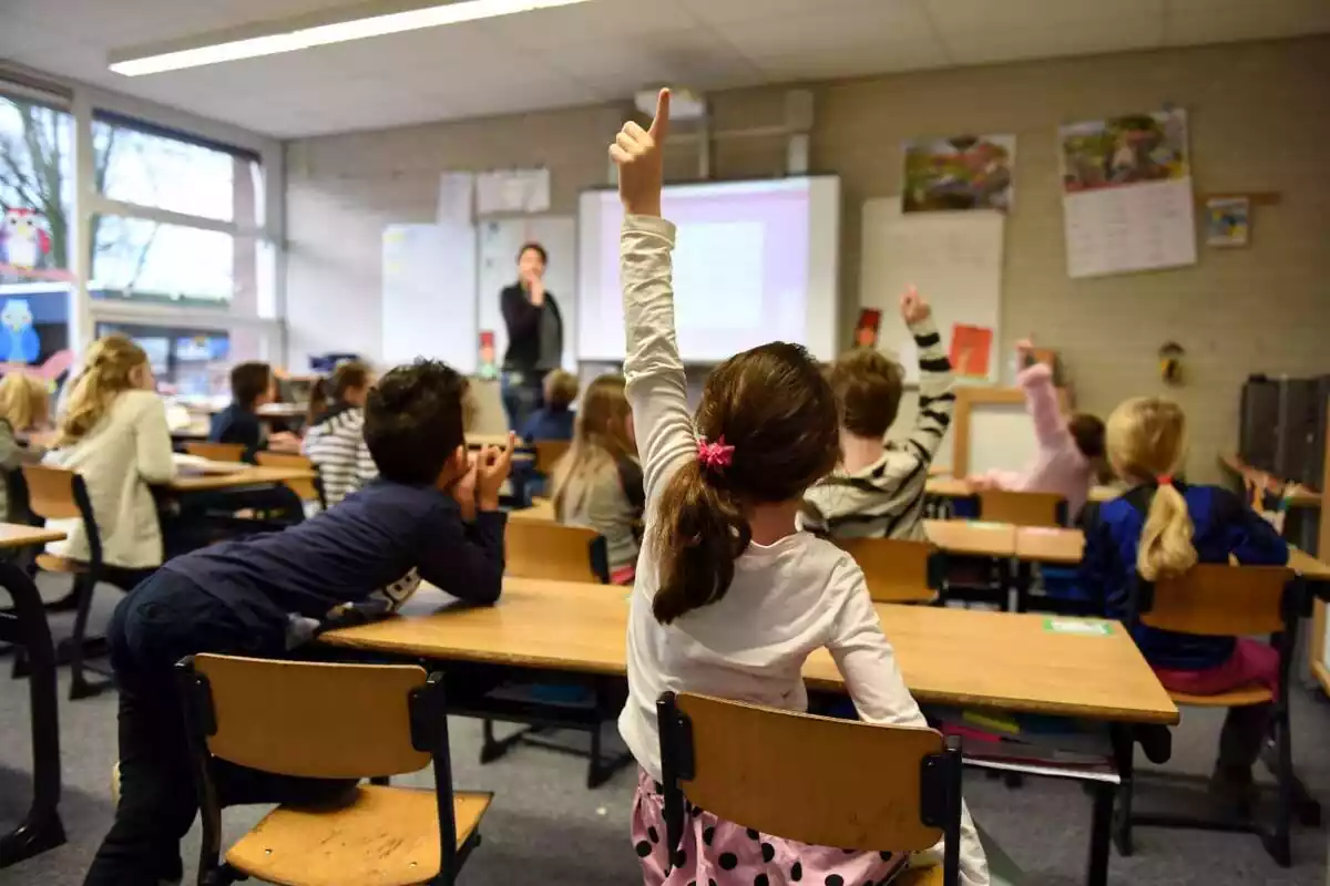 Aula d'una escola amb alumnes de primària aixecant el braç