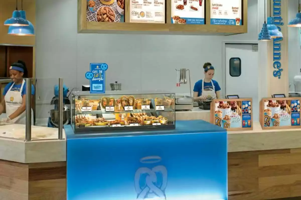 Counter of a pretzel shop with two employees preparing products and a display case filled with different types of pretzels and snacks Counter of a pretzel shop with two employees preparing products and a display case filled with different types of pretzels and snacks