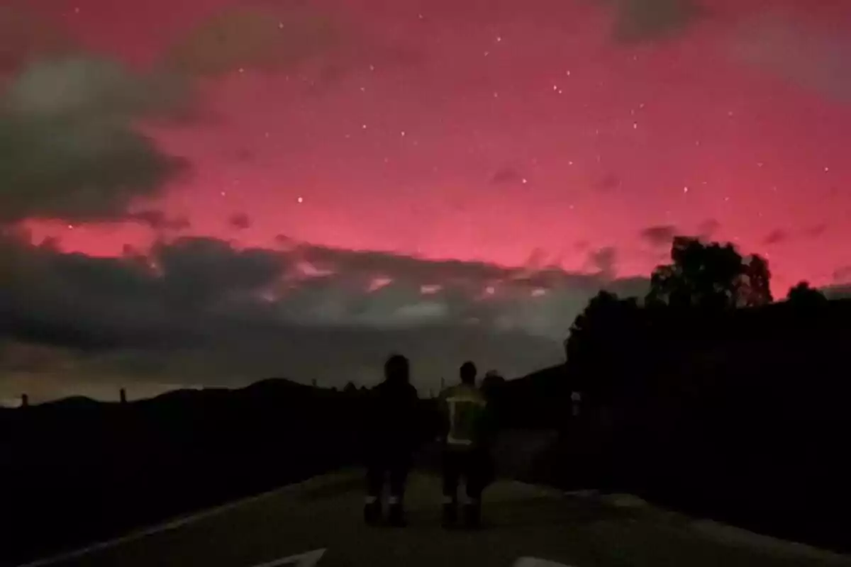 Two people standing on a road looking at a night sky with a red glow and dark clouds. Two people standing on a road looking at a night sky with a red glow and dark clouds.
