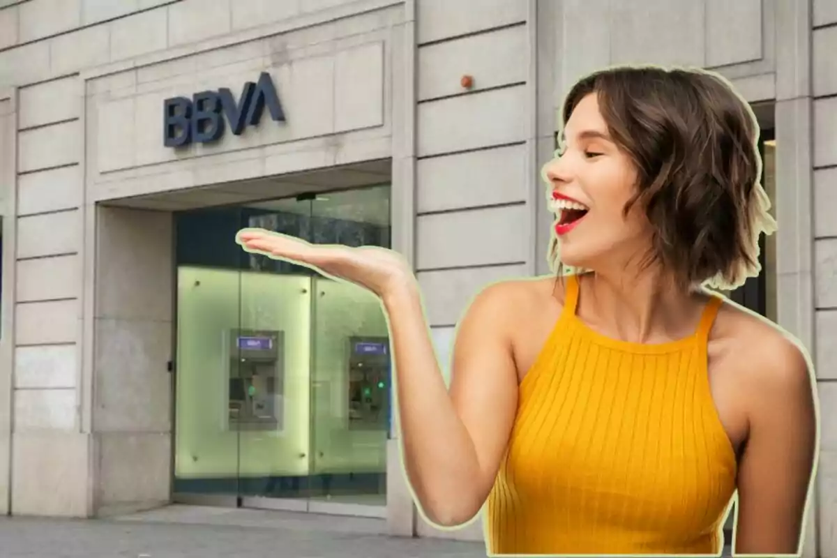 Smiling woman in yellow dress extends her hand in front of BBVA bank branch.