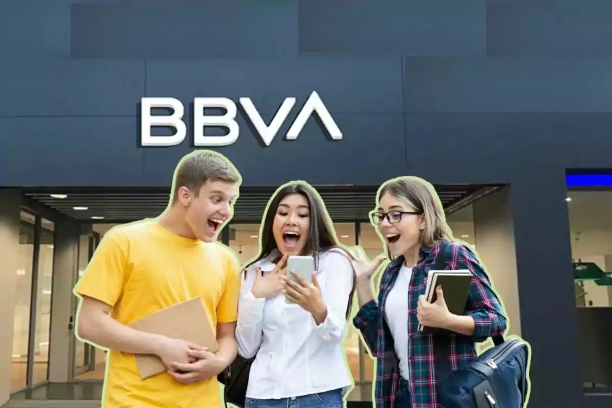 Tres persones joves emocionades mirant un telèfon mòbil davant d'una sucursal del banc BBVA.