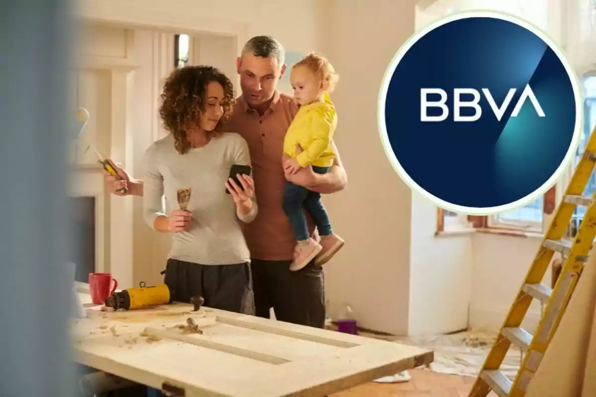 Una família revisa un telèfon mòbil mentre realitza renovacions a casa seva, amb eines i una escala al seu voltant, i el logotip de BBVA a la cantonada superior dreta.