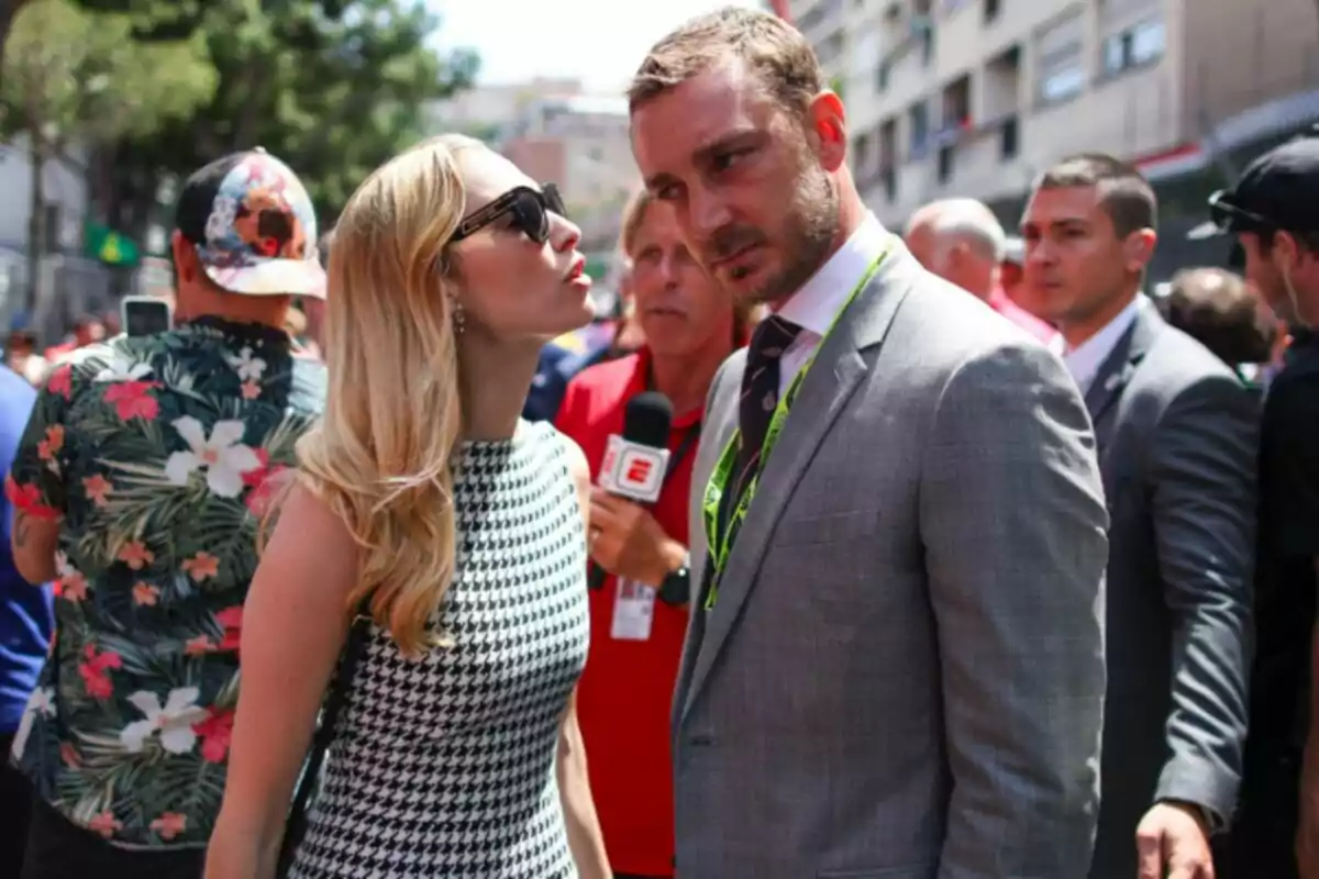 Beatrice Borromeo in sunglasses and a checkered dress talks with Pierre Casiraghi in a suit at an outdoor event, while a reporter holds a microphone in the background. Beatrice Borromeo in sunglasses and a checkered dress talks with Pierre Casiraghi in a suit at an outdoor event, while a reporter holds a microphone in the background.