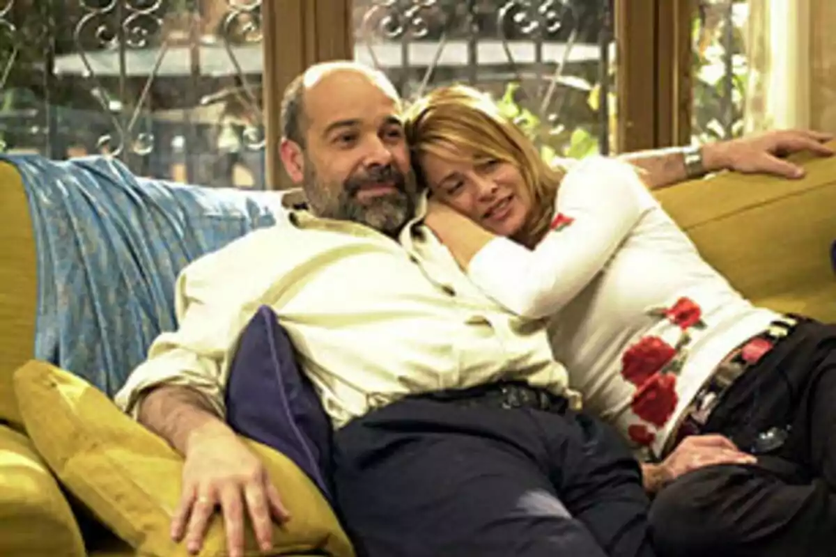 Antonio Resines and Belen Rueda sit on the couch, hugging and smiling in a scene from the movie 