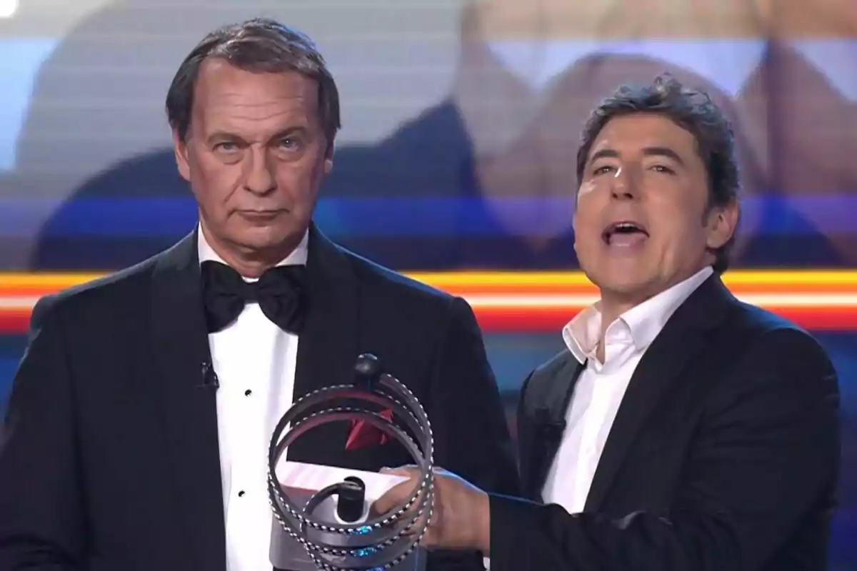 Dos homes en un escenari, Manel Fuentes sosté un objecte circular mentre Bertín Osborne porta un esmòquing i corbata de llaç a Tu Cara Me Suena. Dos homes en un escenari, Manel Fuentes sosté un objecte circular mentre Bertín Osborne porta un esmòquing i corbata de llaç a Tu Cara Me Suena.