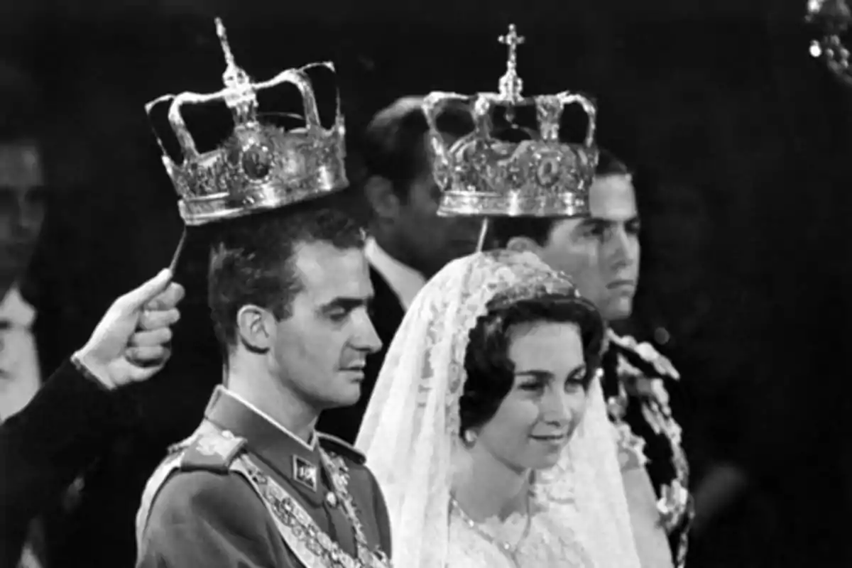 Joan Carles I i la reina Sofia vestida de manera formal estan en una cerimònia, amb corones sostingudes sobre els seus caps. Joan Carles I i la reina Sofia vestida de manera formal estan en una cerimònia, amb corones sostingudes sobre els seus caps.